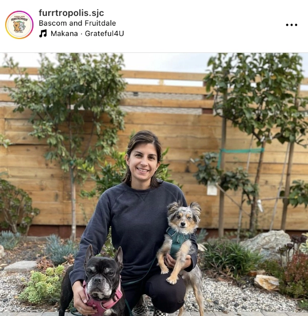 A woman posing with two dogs in a garden.