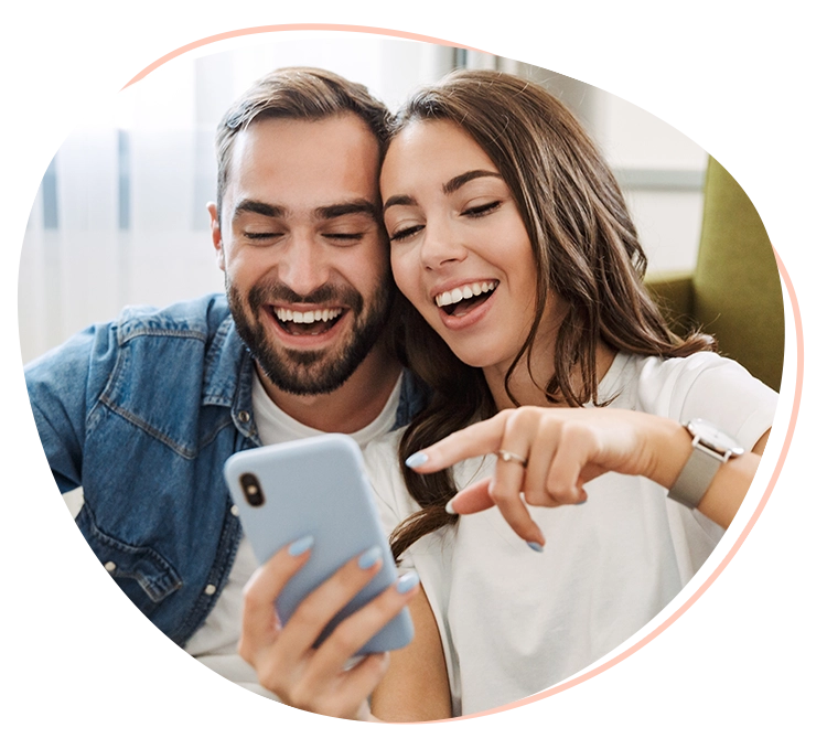 A man and woman laughing while looking at a cell phone.